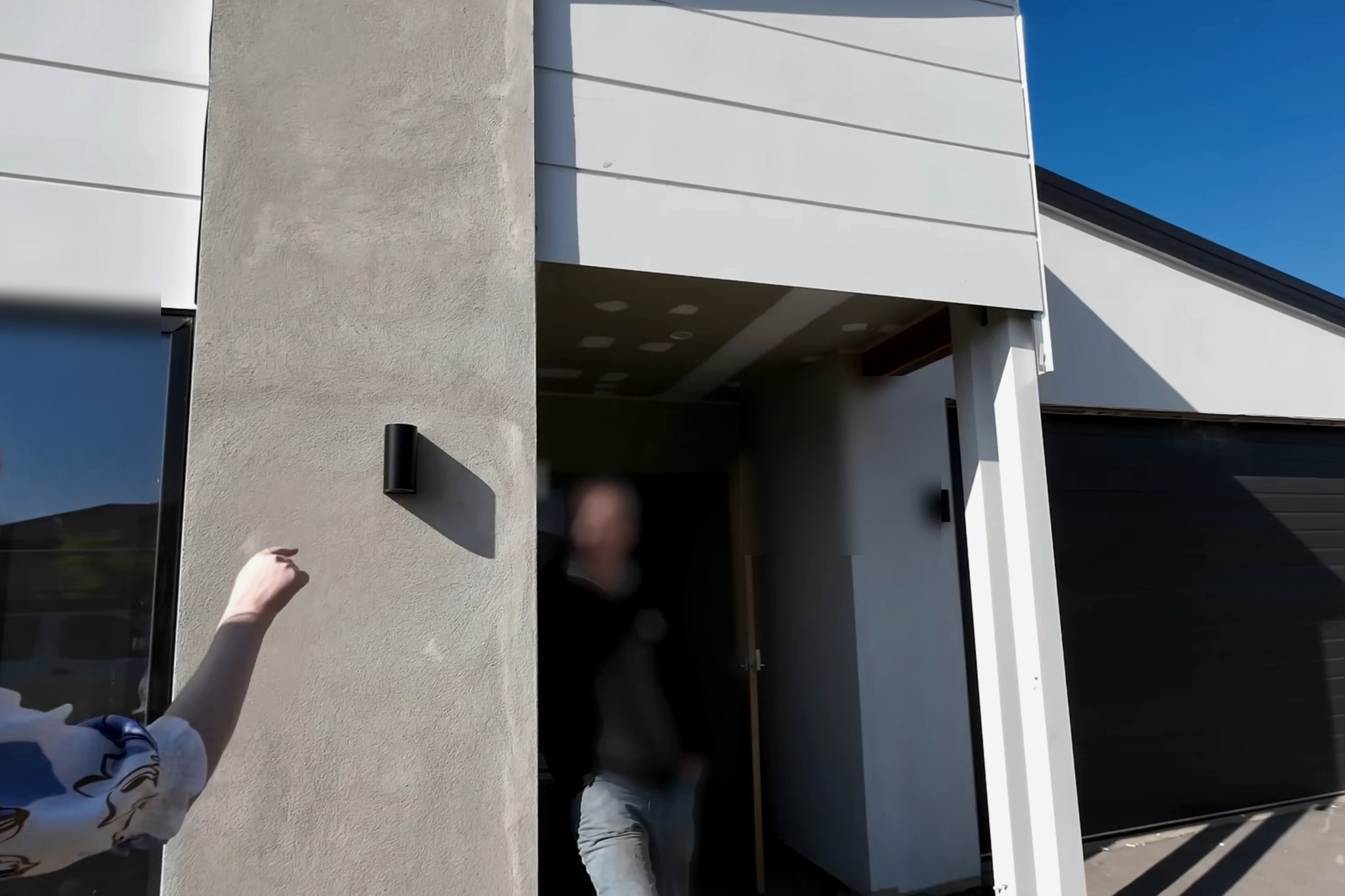 Site Inspections investigation: homeowner pointing at exterior rendering at the affected property, with a figure in the doorway (face blurred for privacy)