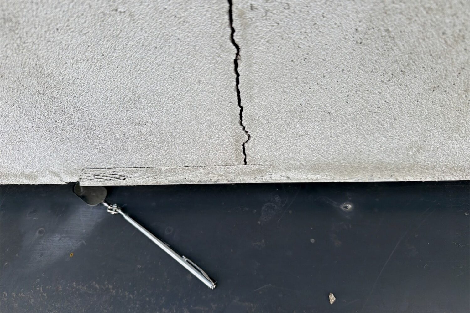 A crack running through a rendered element and opening wider towards the edge, with an inspection probe alongside for scale