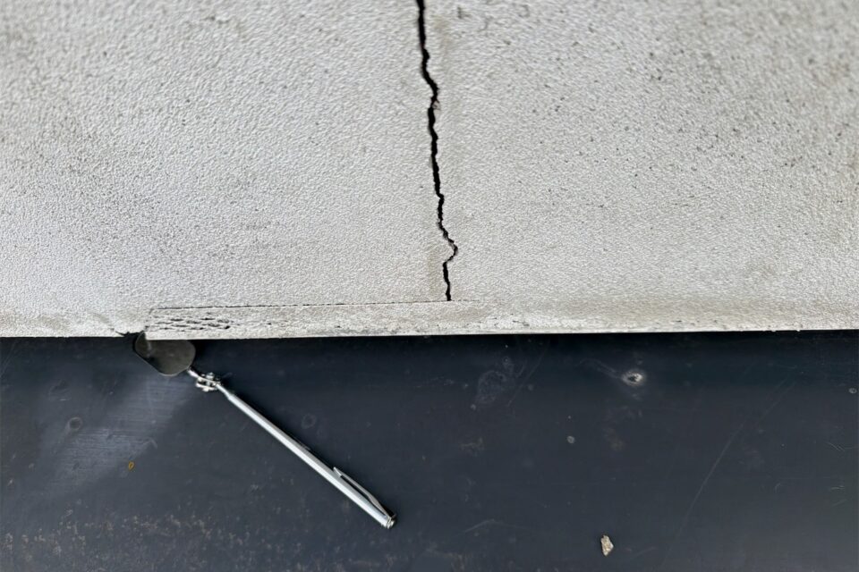 A crack running through a rendered element and opening wider towards the edge, with an inspection probe alongside for scale