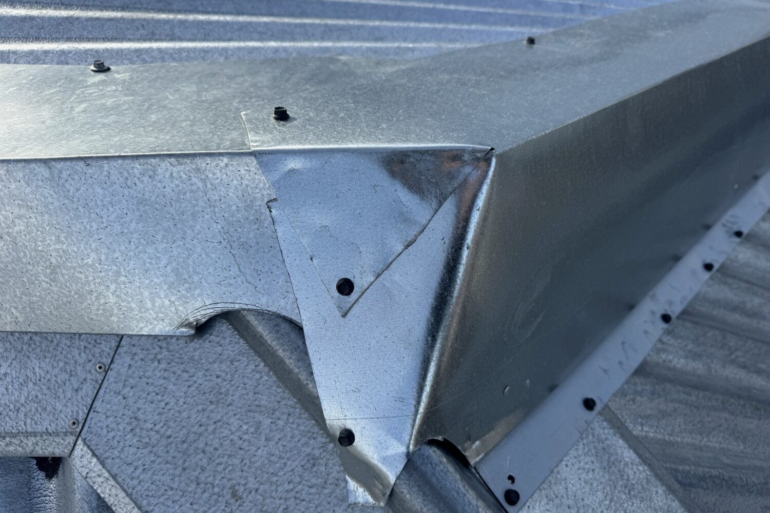 A folded sheet metal flashing junction where roof capping meets the barge, with fixings visible
