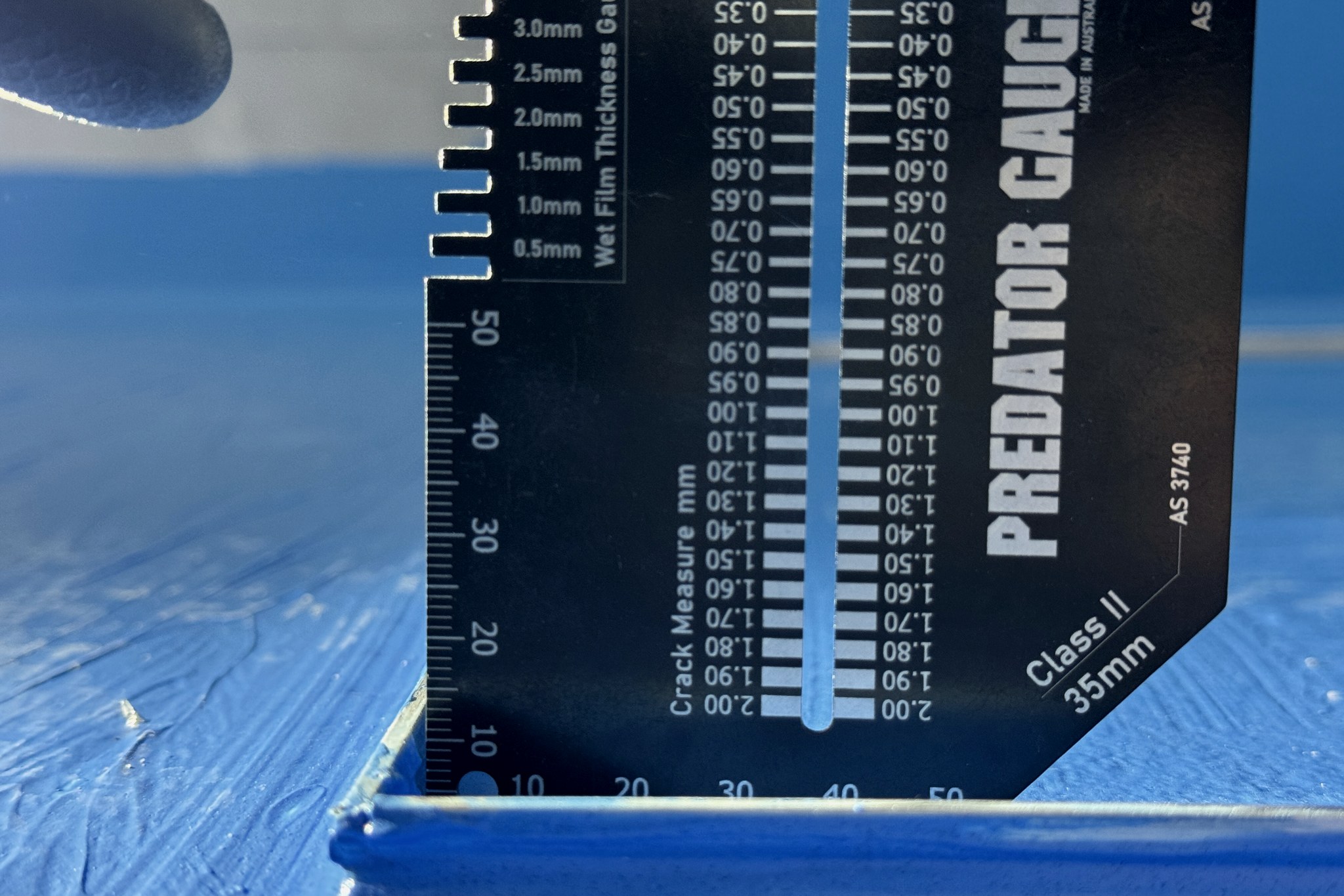 A gauge marked AS 3740 laid across a waterproofing membrane to measure wet film thickness