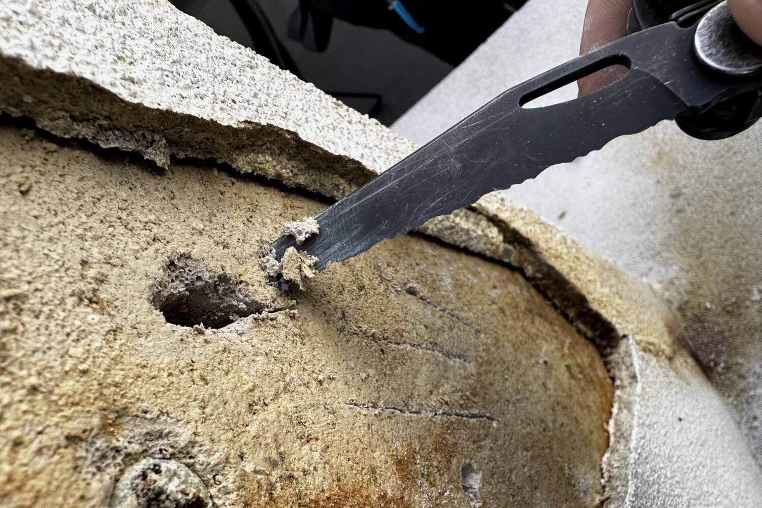 An inspector's blade opening a rendered surface to reveal the substrate beneath during a building inspection