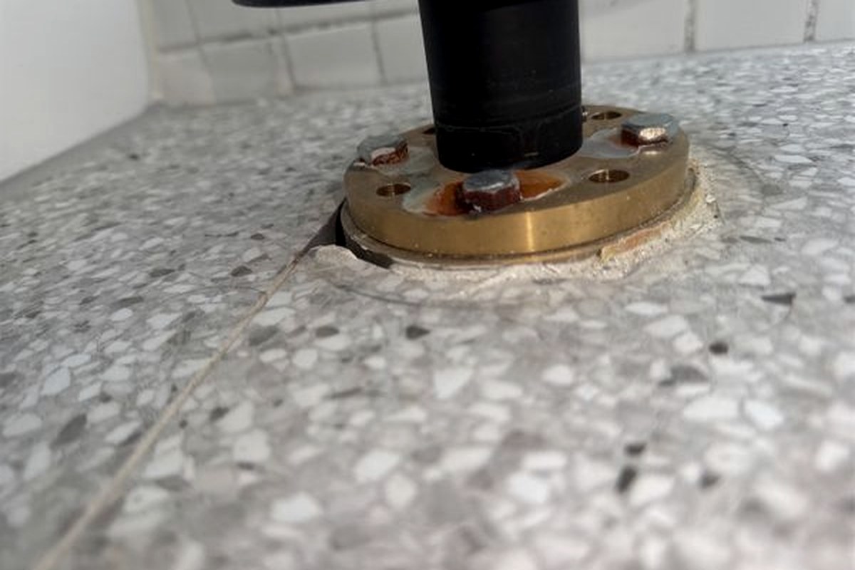 Door stop fixed to a terrazzo wet area floor with a brass base plate, a crack running away from the fixing and staining around the screw heads