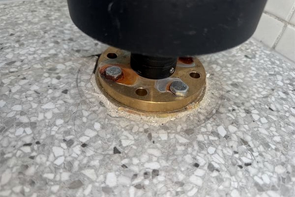 Close view of the door stop base plate showing corrosion staining around the screw heads penetrating the wet area floor