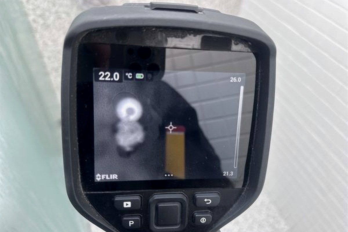 Thermal imaging camera screen showing a bright isolated spot against a cooler surrounding field on a stone wall surface
