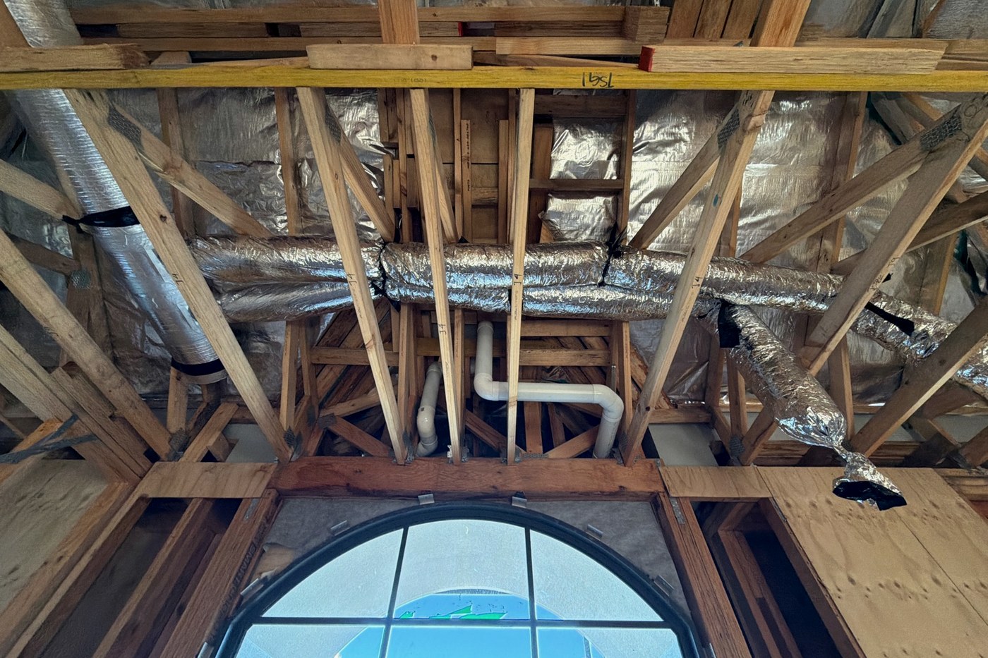 Timber roof trusses and wall bracing with ducting and plumbing penetrations running through the frame of a new house