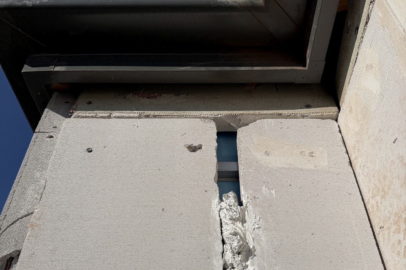 An open vertical joint between cladding sheets beside a window, exposing the steel frame behind, on a home presented as at lock-up