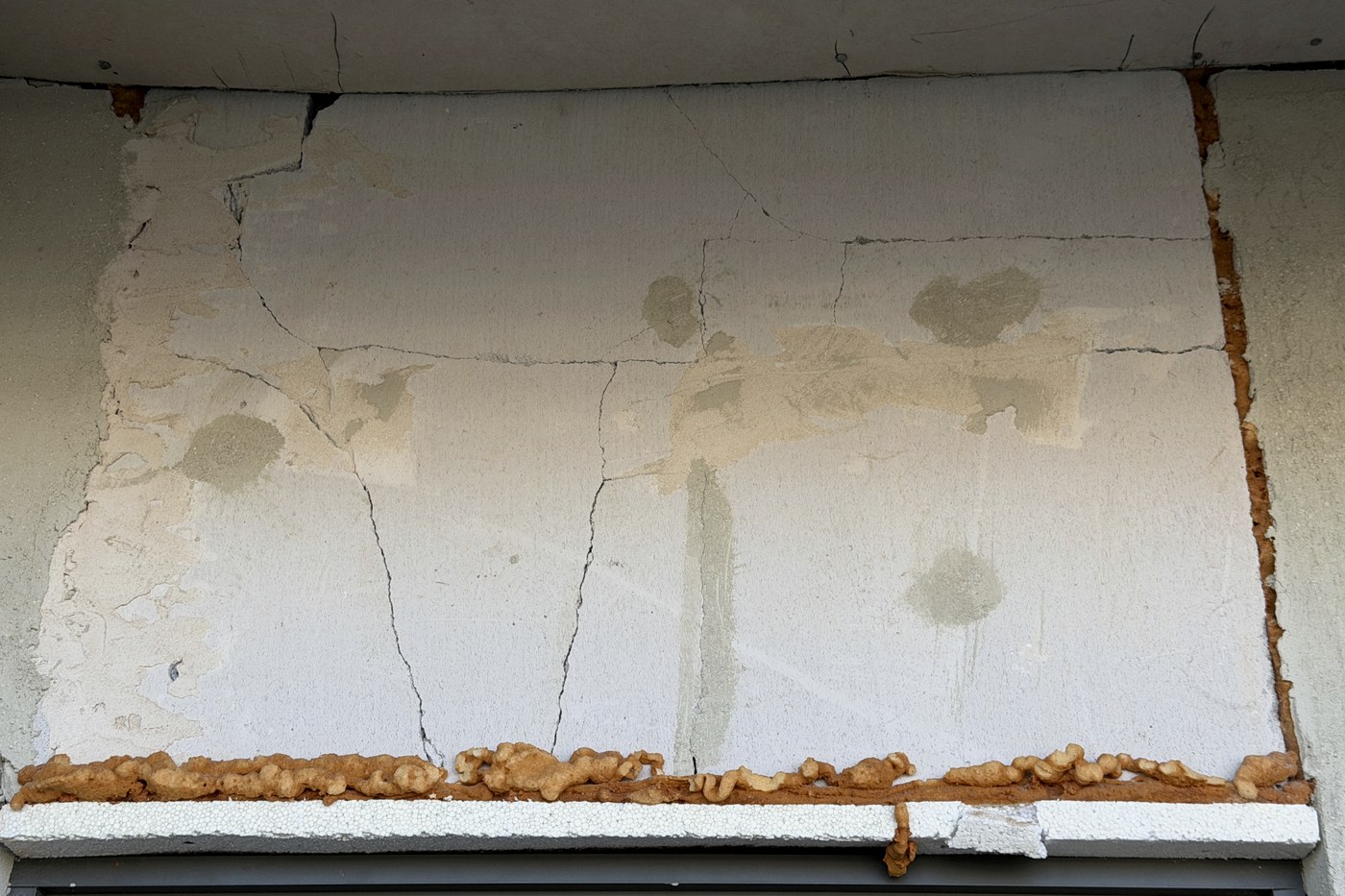Cracked and patched render above a window with expanding foam left protruding, on a home offered for handover as complete