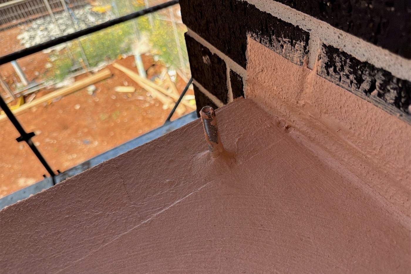 A threaded balustrade fixing penetrating a balcony waterproofing membrane before tiling, leaving an unsealed penetration